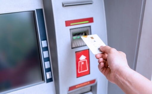 ATMにクレジットカードを挿入する手元。金融機関向けATMシステムやキャッシュレス決済技術の安全性と利便性を支えるソフトウェアソリューション。