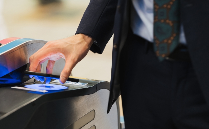 駅の自動改札機にスマートフォンをかざして通過するビジネスマン。ICカード対応の駅務機器システムの利用シーン。