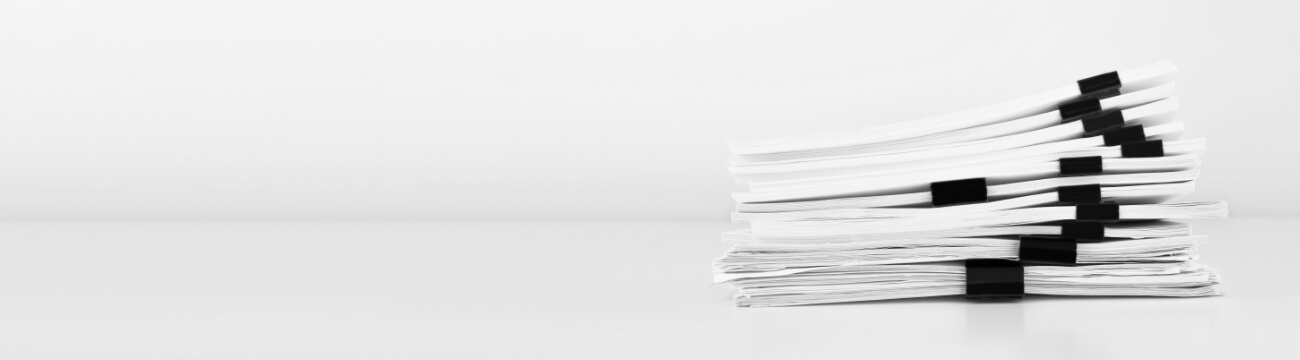 白いデスクに積み重ねられた複数の書類束。オムロン デジタルのコラム記事や技術資料を象徴するイメージ