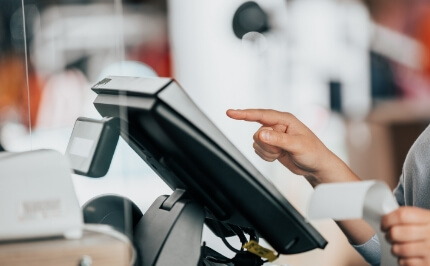 A hand operating the touch panel of a POS system. Part of a POS solution for cash register accounting and self-checkout.
