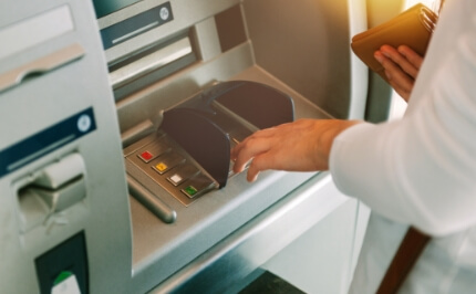 A user's hand operating an ATM. Highly reliable software solutions that support ATMs and financial equipment installed in banks and convenience stores nationwide.