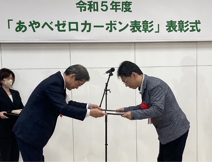 山﨑　善也綾部市長（左）から表彰状を受け取る 綾部工場 生産管理部　部長 河野　雅行(右)