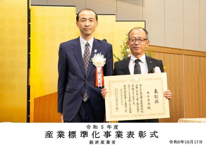 12月13日に開催された贈賞式にて、日刊工業新聞社　代表取締役社長の井水 治博氏（左）より、オムロン株式会社 執行役員の神尾 幸孝（右）に記念の賞状が授与されました。
